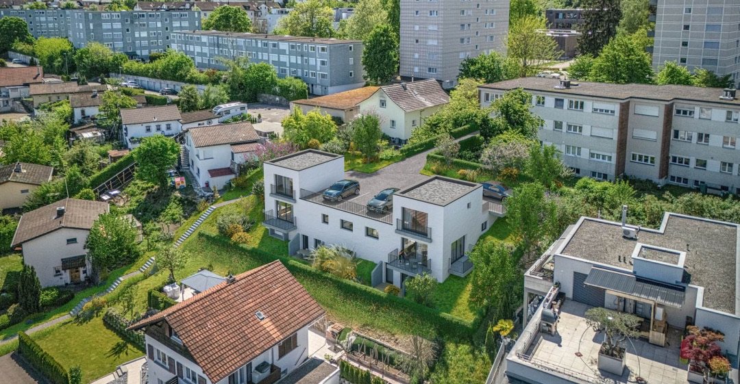 Luftaufnahme des Doppelhauses: zwei weisse Baukörper mit Flachdach, gestaffelten Terrassen und Rasenflächen am Hang